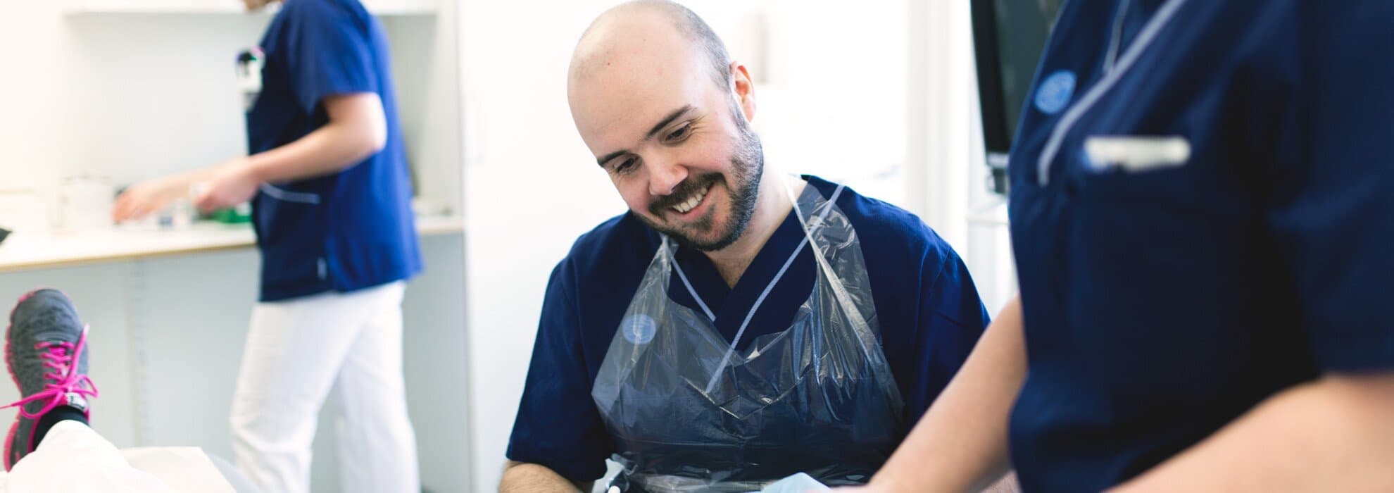 Två medarbetare tar hand om en patient som ligger i sin säng. Två medarbetare tar hand om en patient som ligger i sin säng.