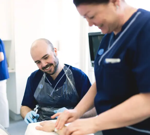 Två medarbetare tar hand om en patient som ligger i sin säng.